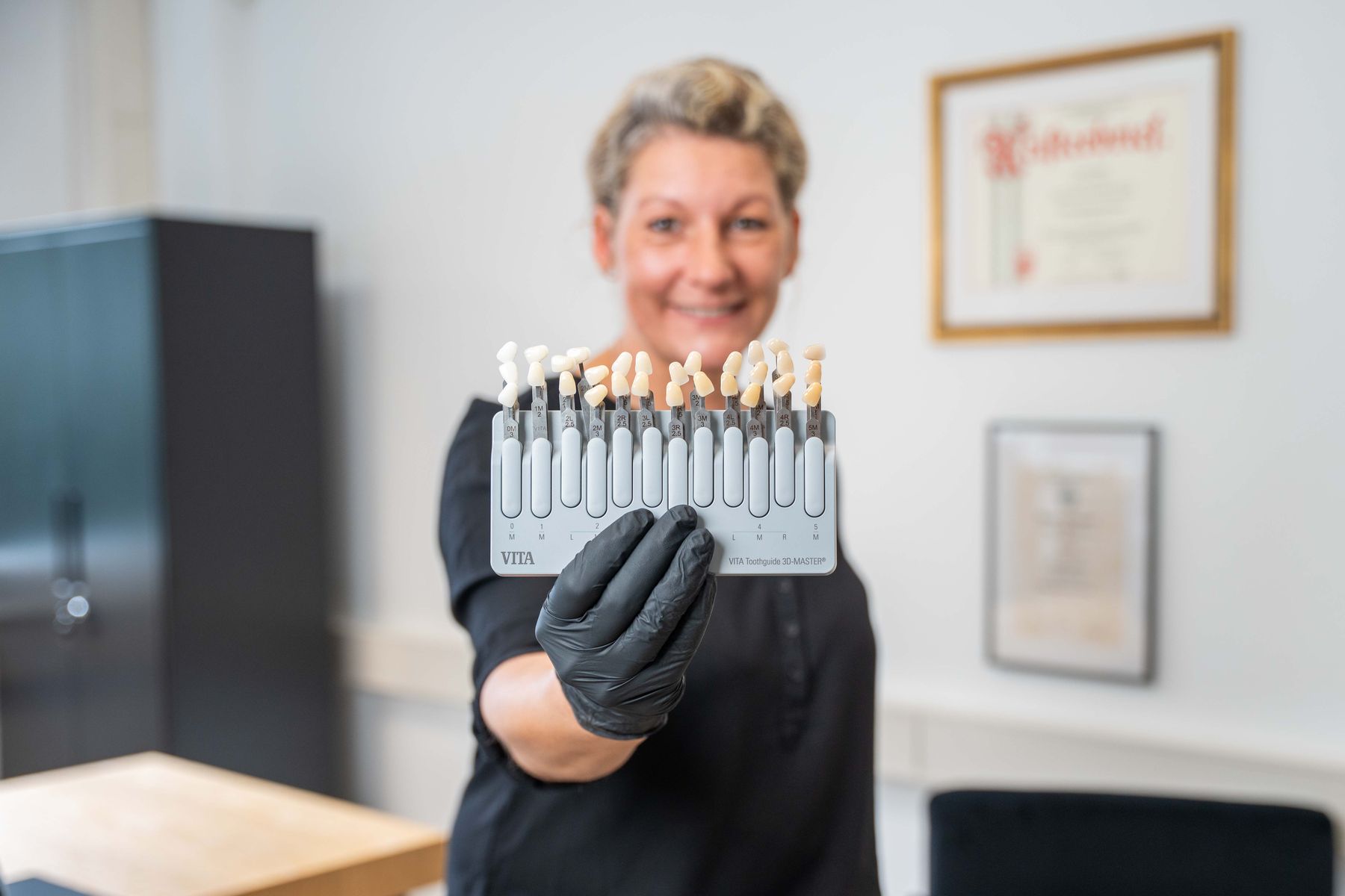 Zahntechnikerin hält einen Farbring zur Bestimmung der Zahnfarbe im Labor